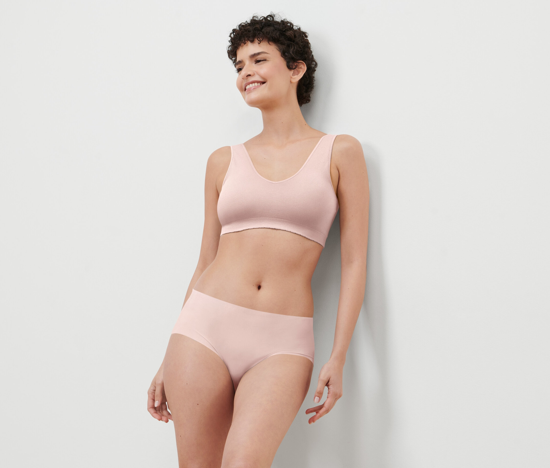 Frau mit kurzen Haaren trägt einen rosa BH und Höschen.