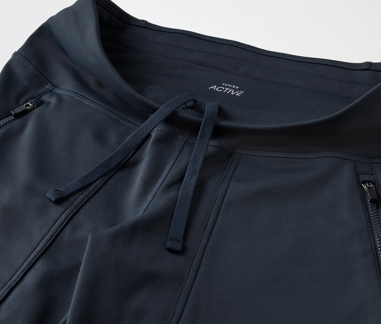 Detailaufnahme einer dunkelblauen Trainingshose mit Reißverschlusstaschen und Kordelzug.