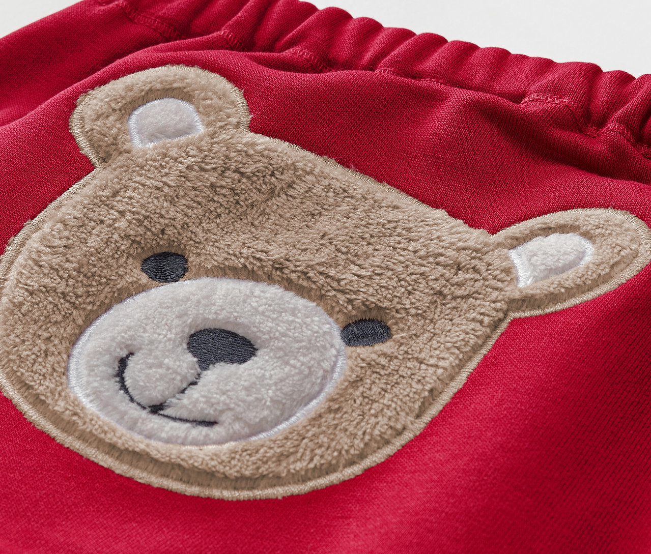Detail einer roten Kinderhose mit braunem Teddybär-Applikation.