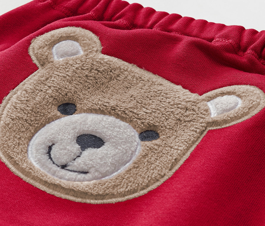 Detail einer roten Kinderhose mit braunem Teddybär-Applikation.
