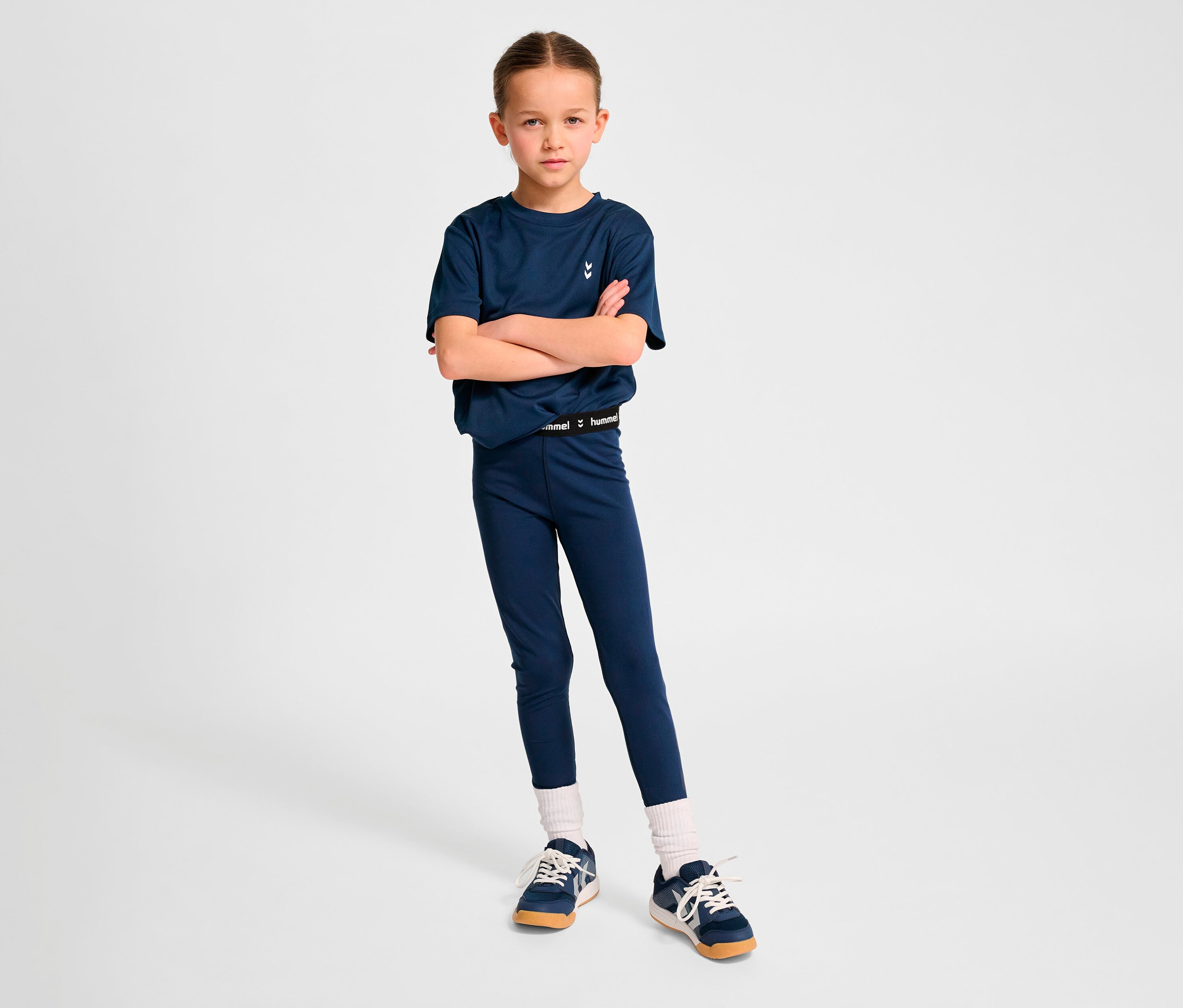 Mädchen posiert mit verschränkten Armen in marineblauem T-Shirt und HUMMEL HMLJR Pulse Mid Waist Tight Leggings.