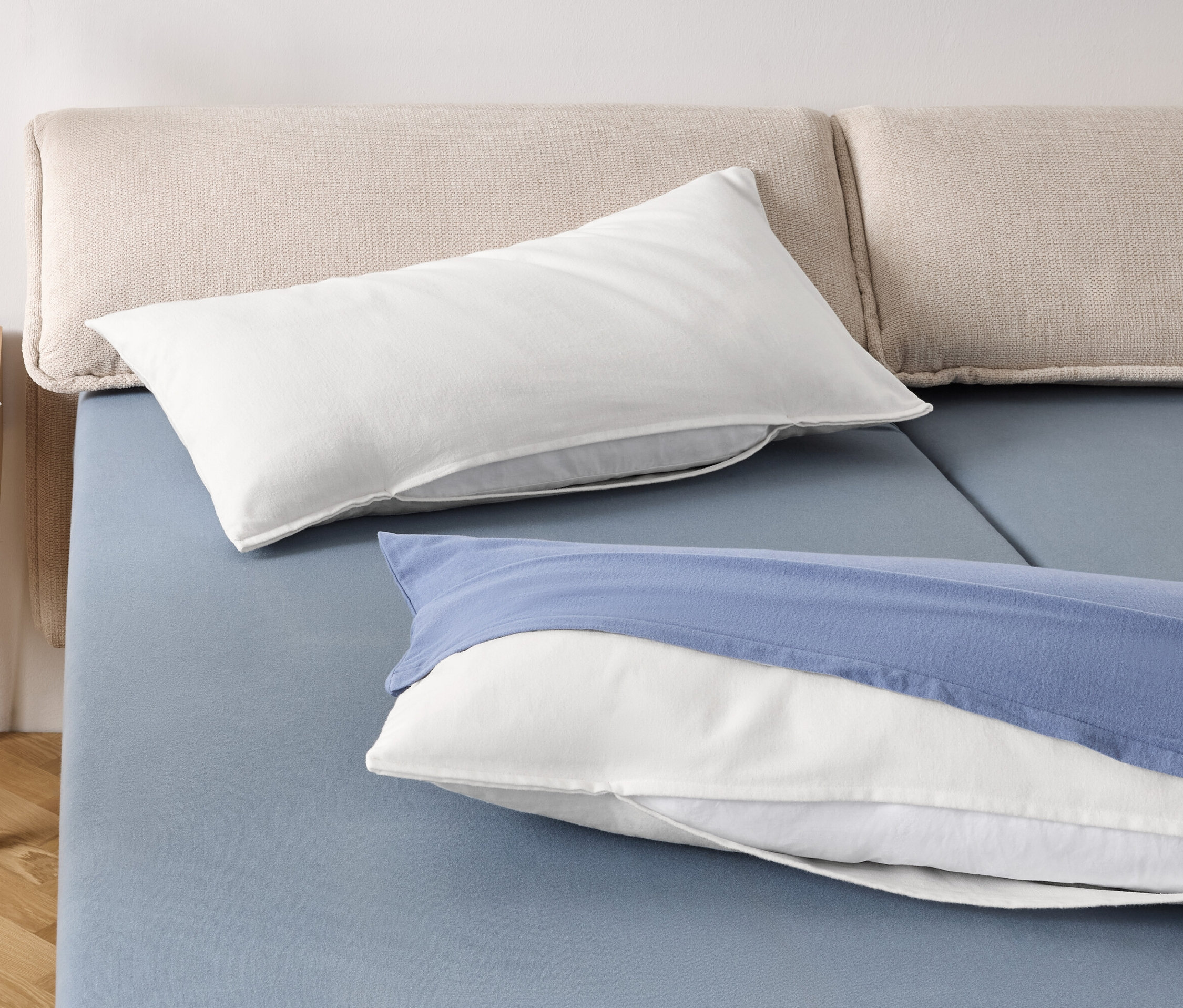 Zwei weiße Kissen und ein weißes Kissen mit blauem Bezug auf einem blauen Bett.