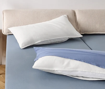 Zwei weiße Kissen und ein weißes Kissen mit blauem Bezug auf einem blauen Bett.