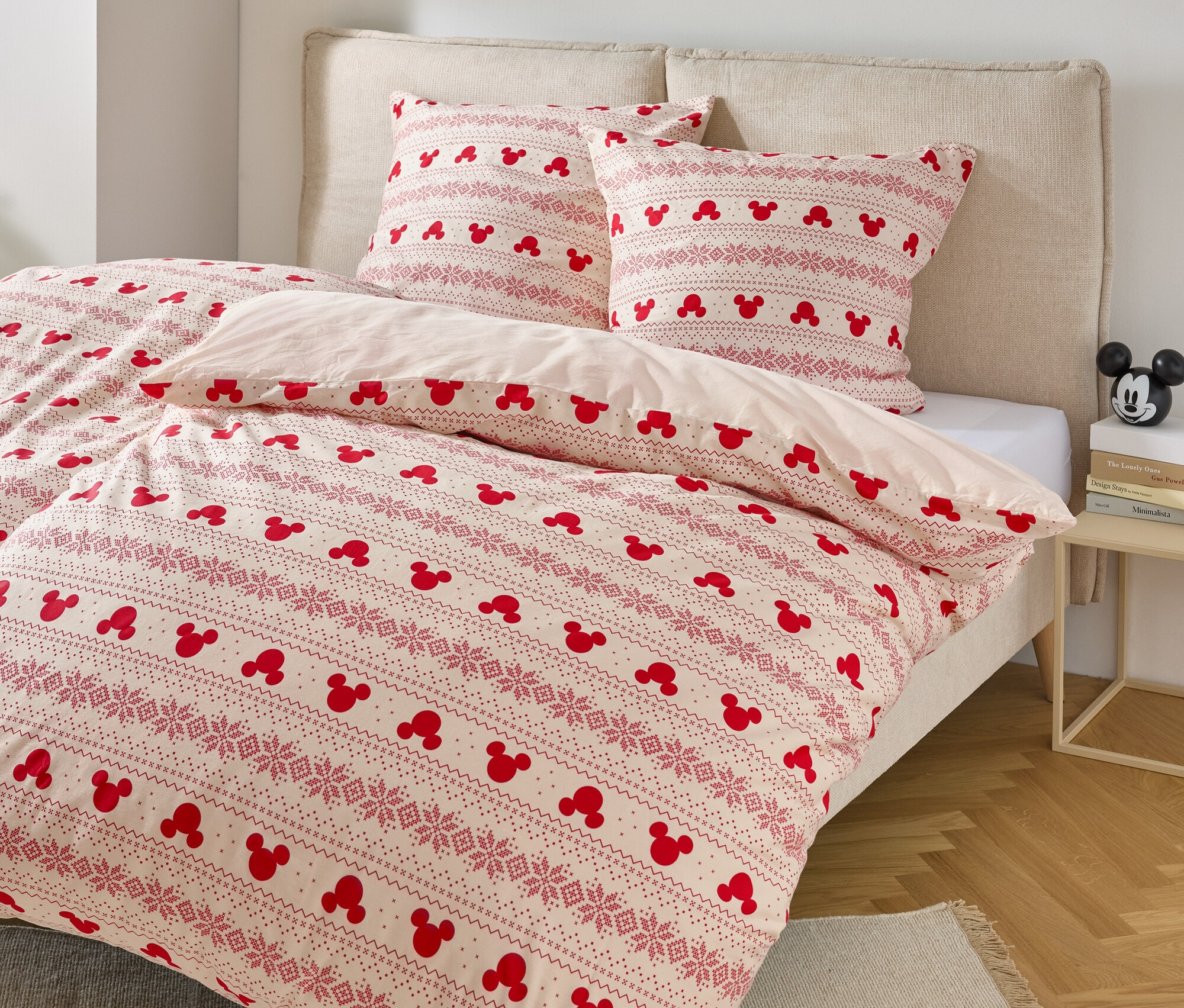 Bett mit Bettwäsche mit Mickey Mouse-Motiv und zwei Kissen mit ähnlichem Muster.