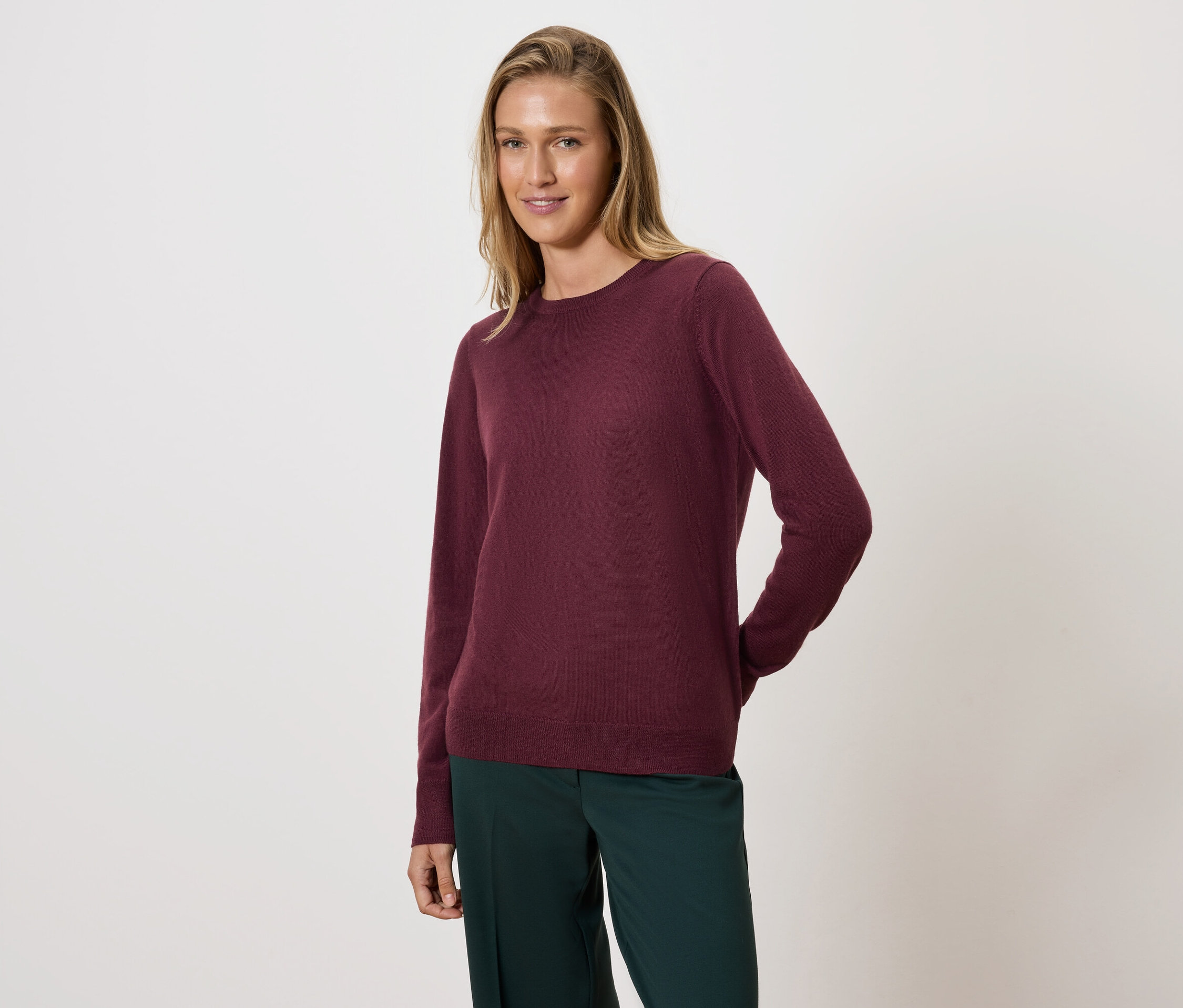 Frau posiert in bordeauxfarbenem Pullover und grüner Hose.
