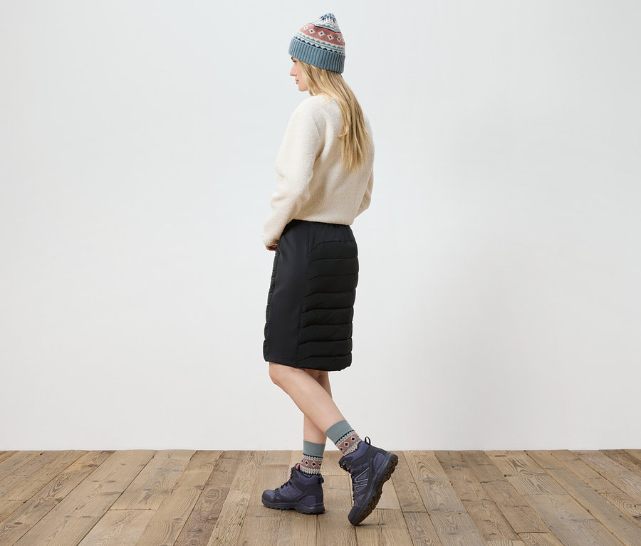 Frau posiert in cremefarbenem Pullover, schwarzem Rock, Stiefeln und Strickmütze.