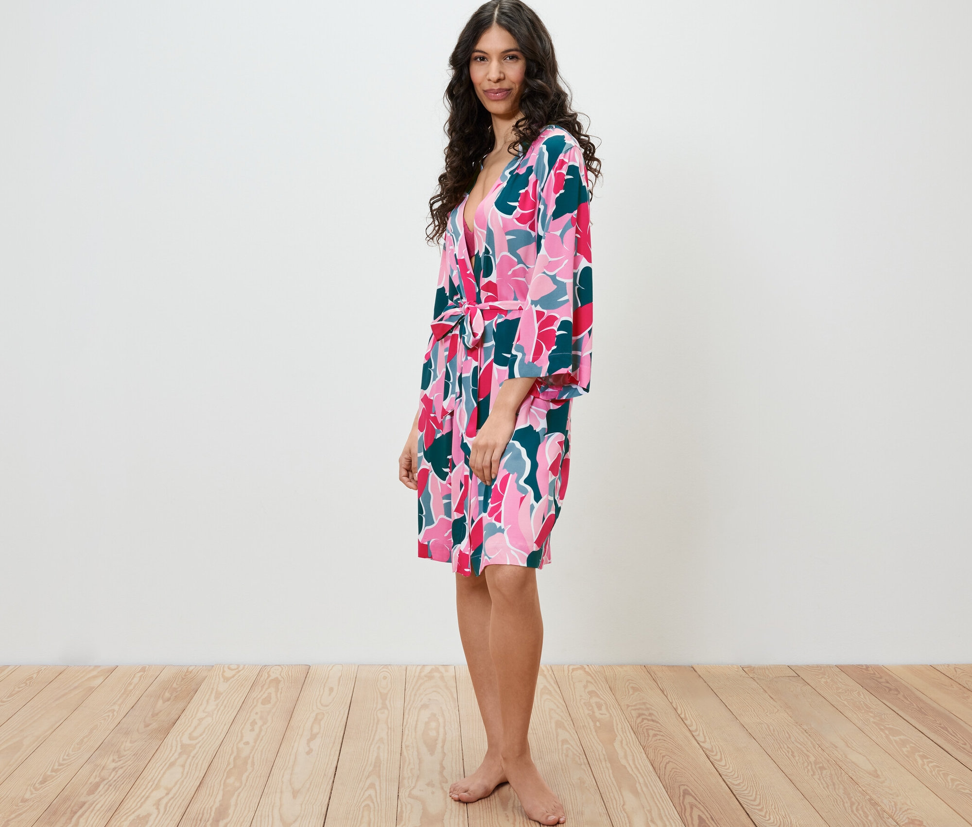 Frau steht seitlich und trägt einen Morgenmantel mit Blumenmuster.