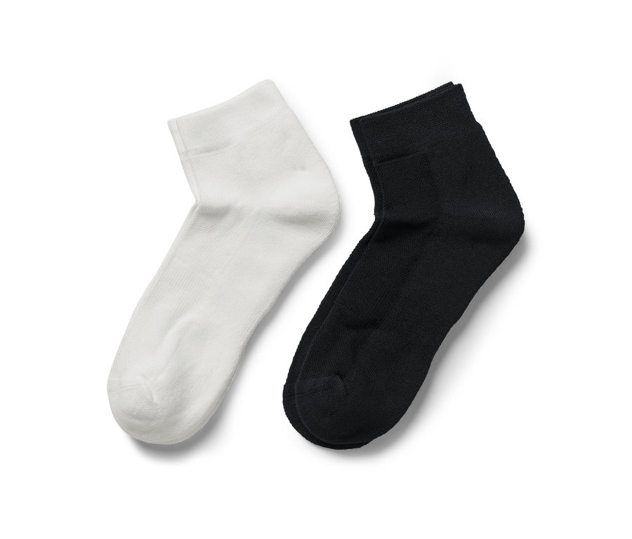 Zwei Paar Sportsocken COOLMAX®, ein Paar weiß, ein Paar schwarz, liegen nebeneinander auf weißem Grund.
