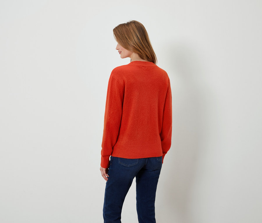 Frau mit orangefarbenem Pullover und dunkelblauen Jeans, die mit dem Rücken zum Betrachter steht.