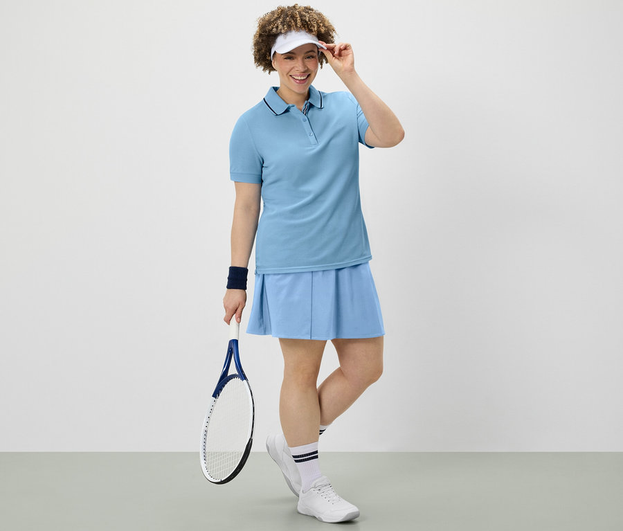 Frau hält Tennisschläger, trägt hellblauen Sportrock und Funktionspoloshirt.