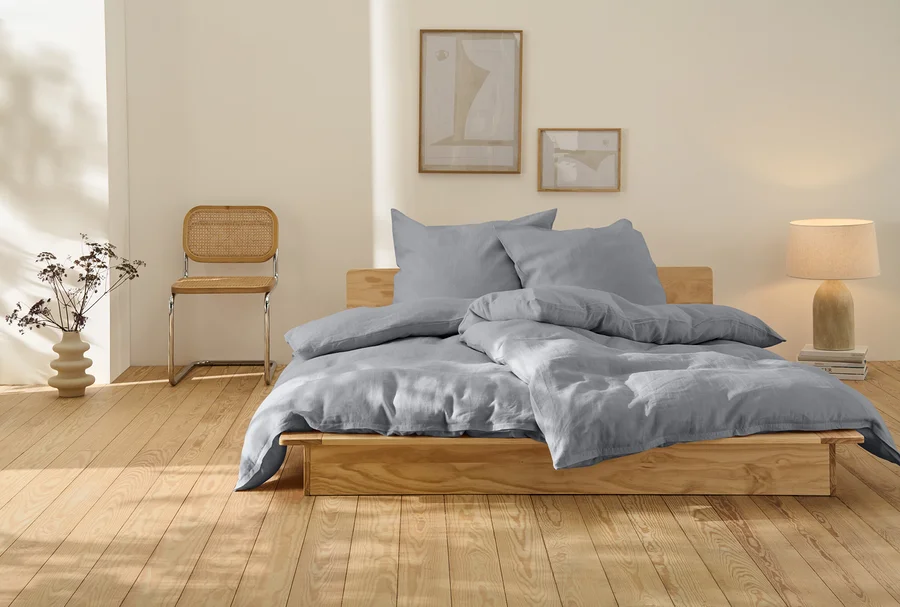 Graue Leinen-Bettwäsche in Übergröße auf einem Holzbett.