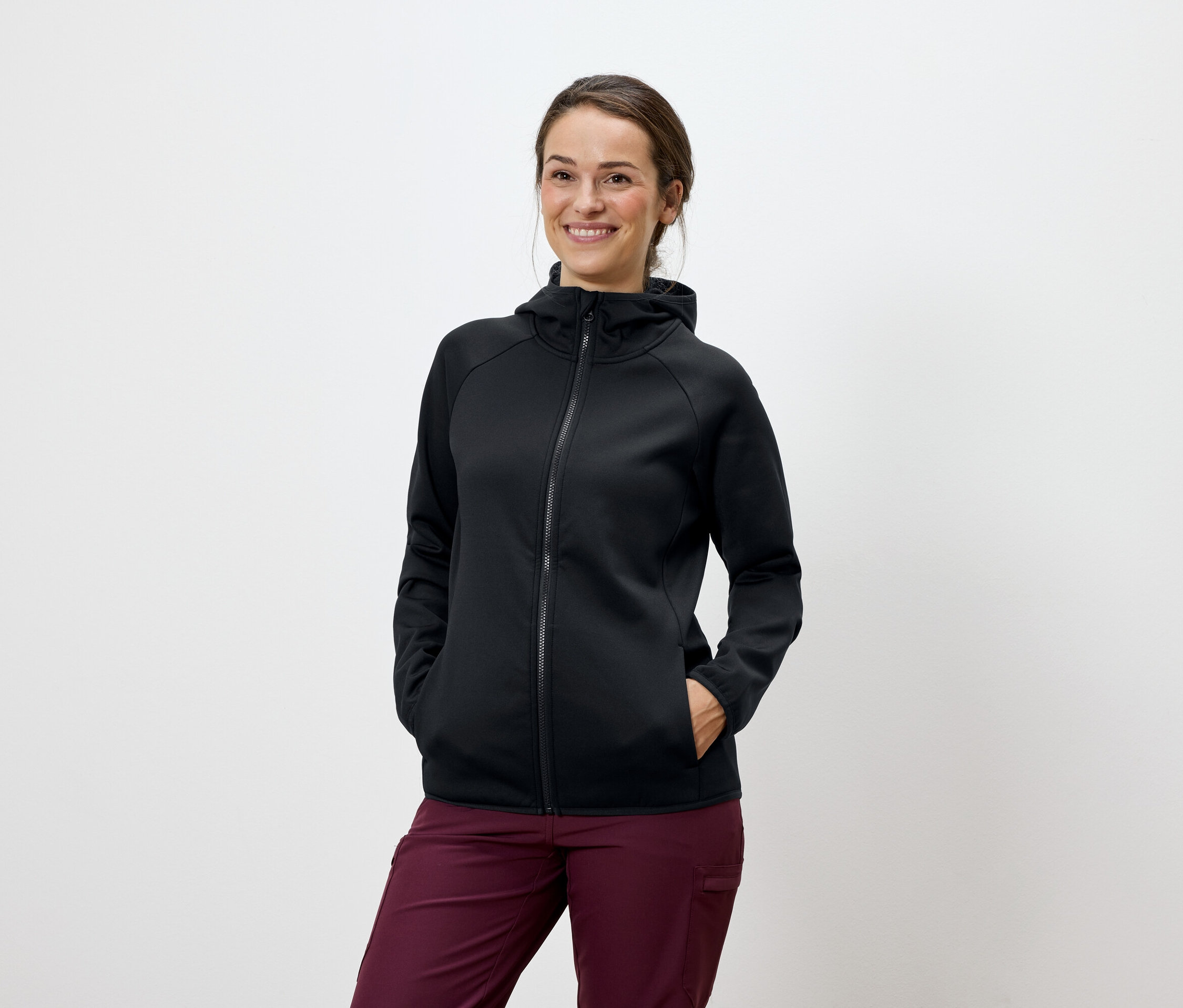 Eine Frau posiert in einer schwarzen Kapuzenjacke und weinroten Hosen.