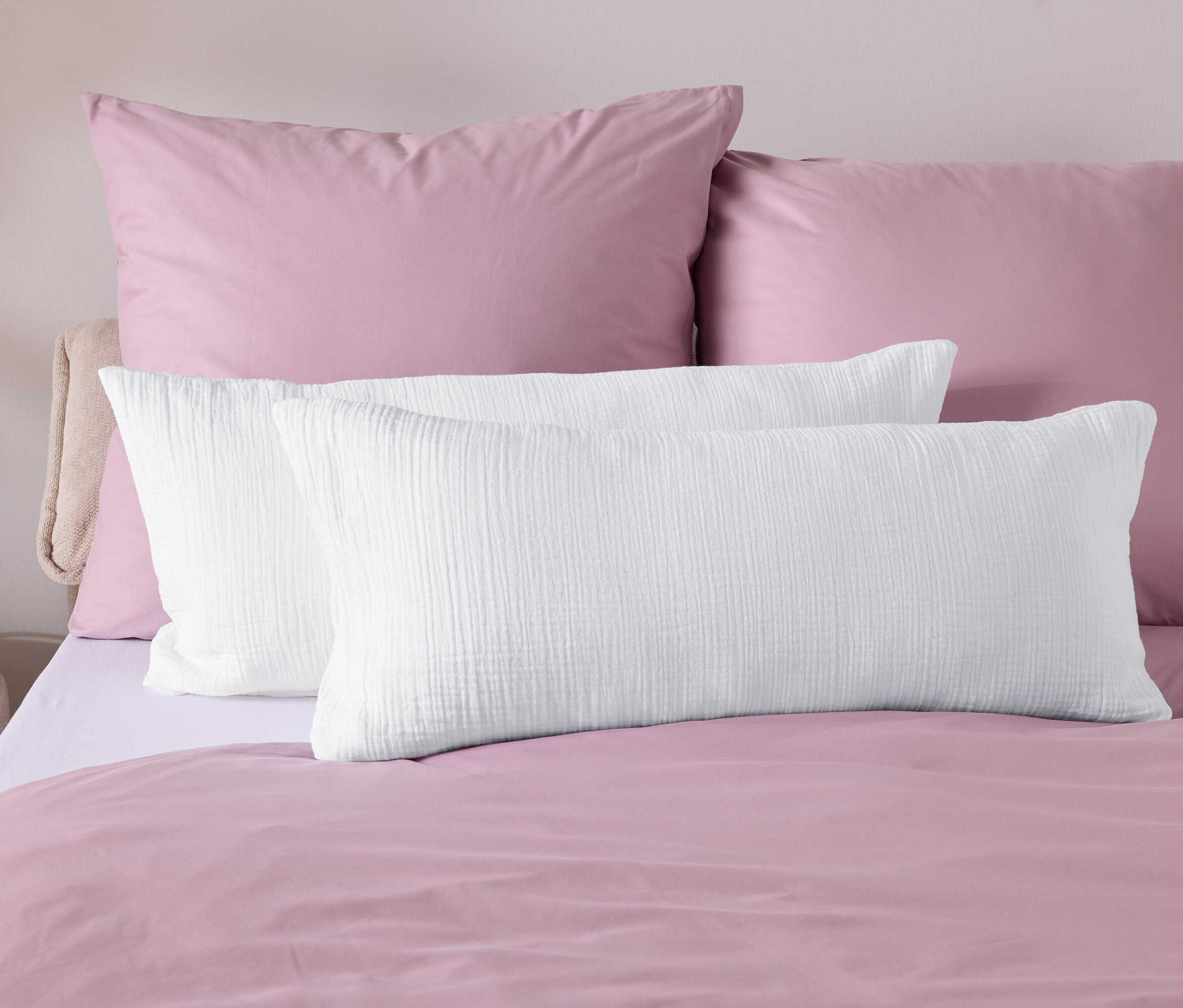 Nahaufnahme von Bettwäsche mit rosafarbener Bettdecke und weißen Kissen.