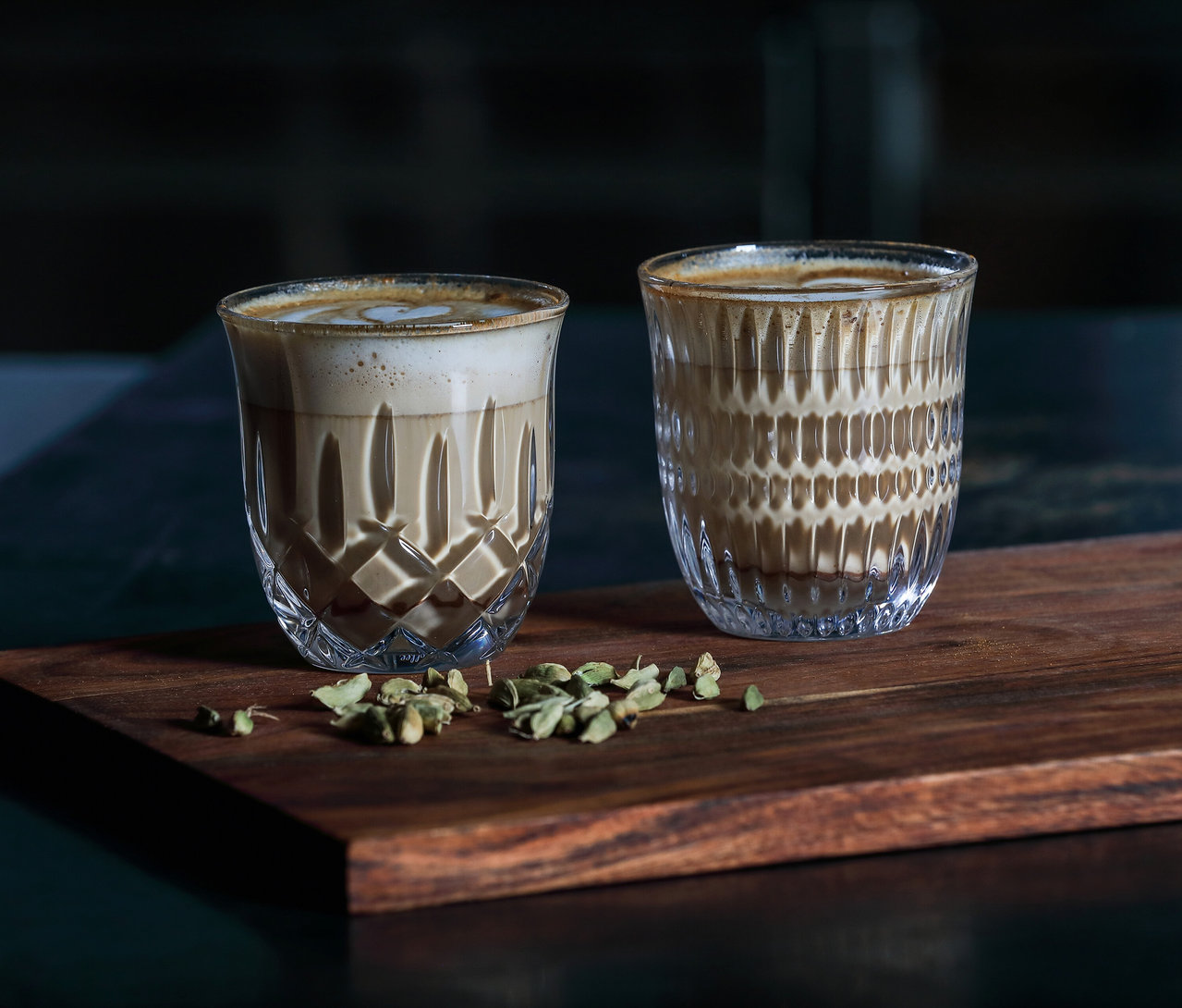 Zwei mit Milchschaum gefüllte Nachtmann Cappuccinogläser »Noblesse« stehen auf einem Holzbrett, verziert mit Kardamom.