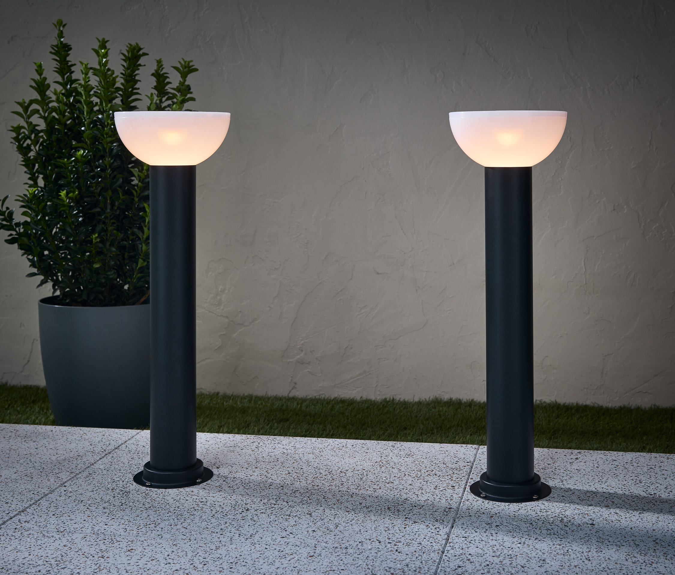 Zwei Solar-Wegleuchten beleuchten einen Weg. Neben einer Lampe steht ein Blumentopf.