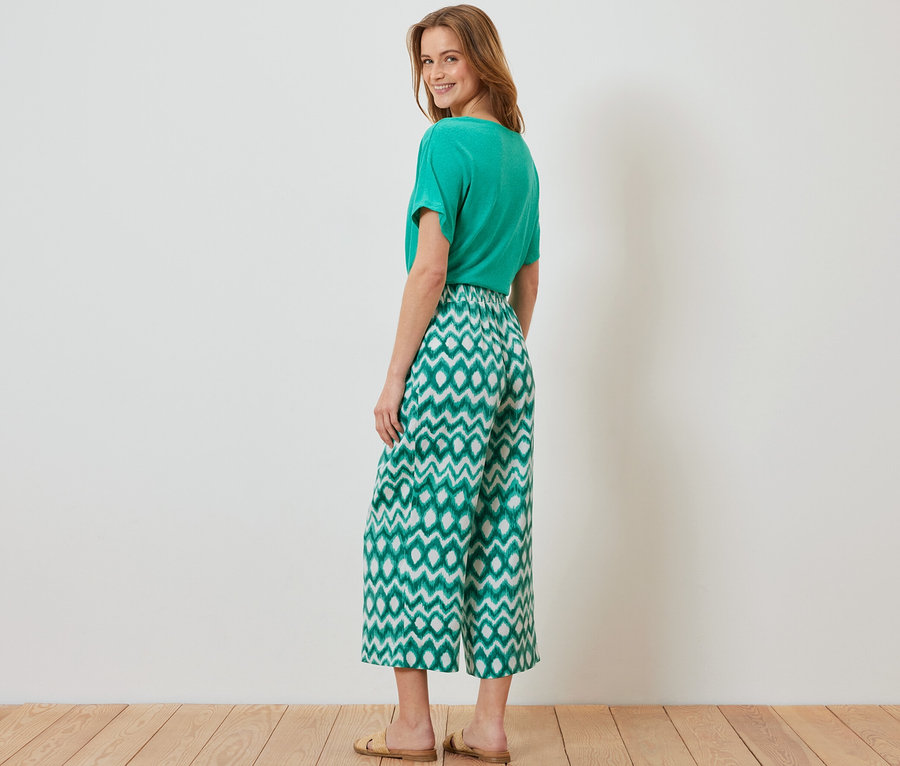 Eine Frau posiert in einem grünen T-Shirt und einer bedruckten Satinhose.