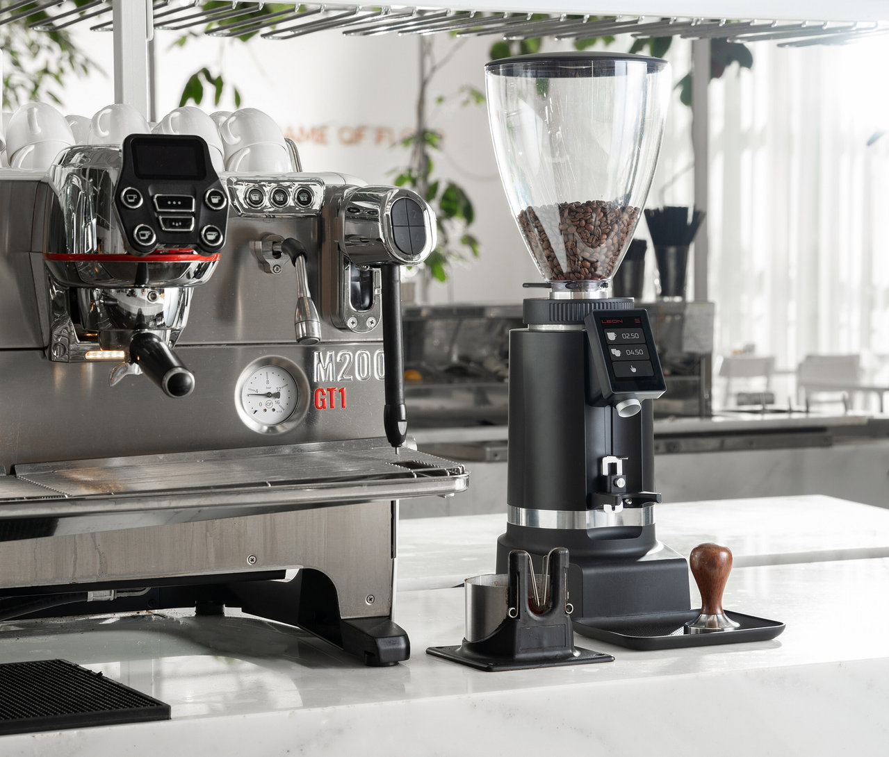 Eine silberne Kaffeemaschine steht neben einer schwarzen Kaffeemühle auf einer weißen Theke.