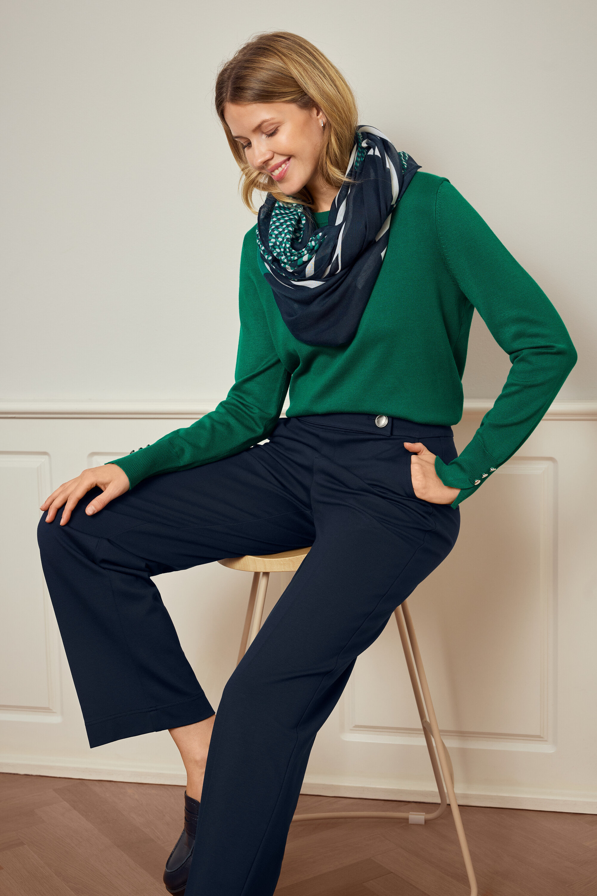 Frau sitzt auf einem Hocker und trägt grüne Oberbekleidung, eine dunkle Hose und 925 Silber Creolen Hexagon.