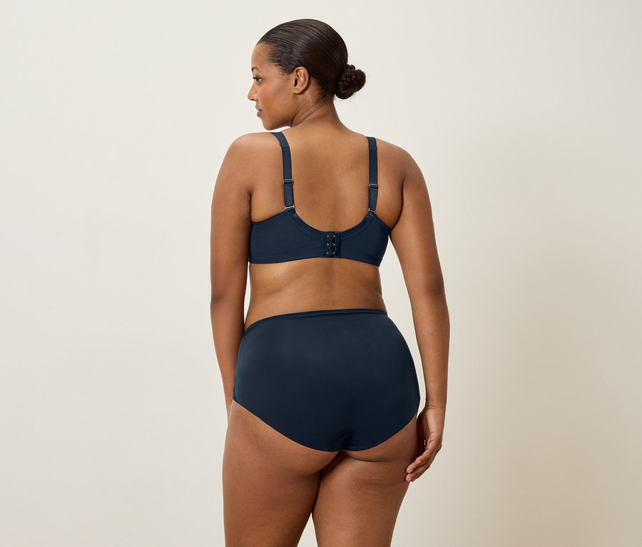 Eine Frau mit dunklen Haaren, von hinten gesehen, trägt einen marineblauen BH und passende Slips.