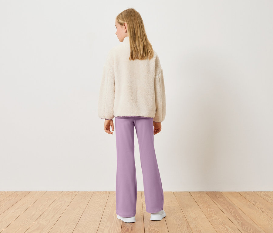 Blick von hinten auf ein blondes Mädchen mit cremefarbenem Teddy-Fleece-Oberteil und lilafarbenen Hosen.