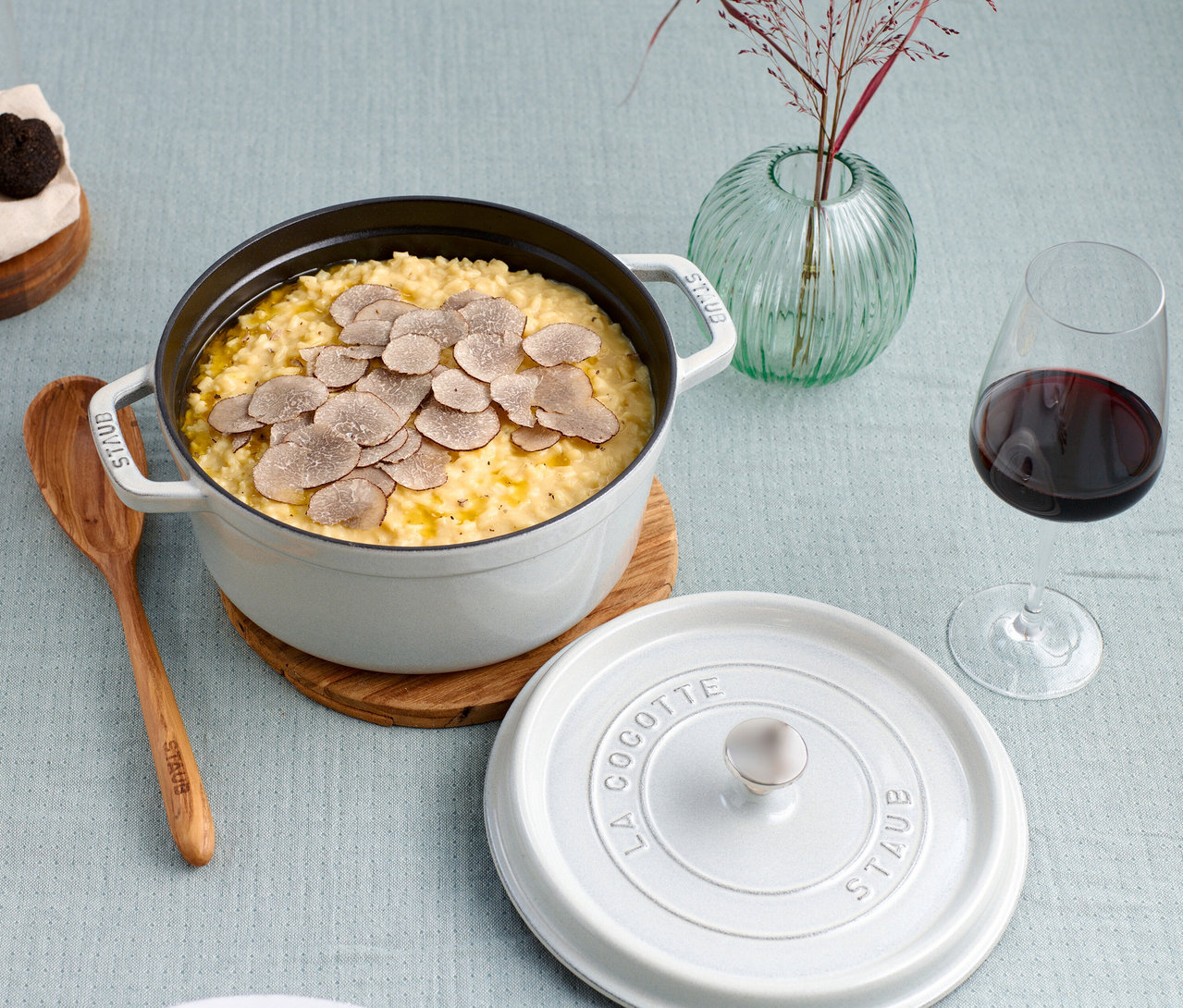 Ein weißer STAUB »Cocotte 24« Topf (ca. 3,7 l) gefüllt mit Risotto und Trüffeln steht auf einem Tisch neben einem Glas Rotwein.