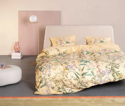 Gelbes Essenza »Augustina« Satin-Bettzeug mit Blumenmuster auf einem Bett mit hellgrauem Kopfteil.