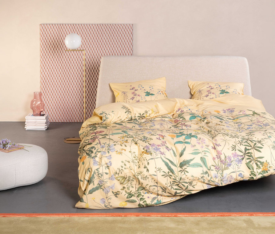 Gelbes Essenza »Augustina« Satin-Bettzeug mit Blumenmuster auf einem Bett mit hellgrauem Kopfteil.