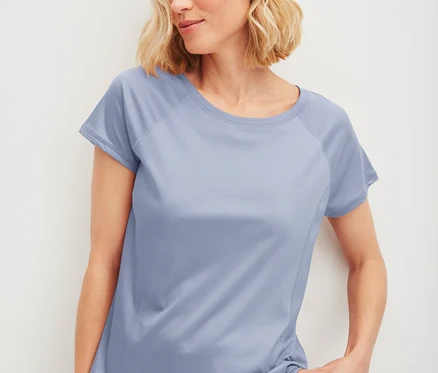 Blonde Frau trägt ein hellblaues CALIDA DEEPSLEEPWEAR kühlendes Kurzarm-Shirt und hält den Saum fest.
