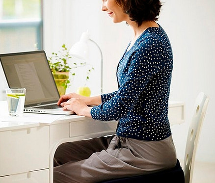 Frau sitzt am Schreibtisch und benutzt einen Laptop auf einem TEMPUR® Keilsitzkissen.