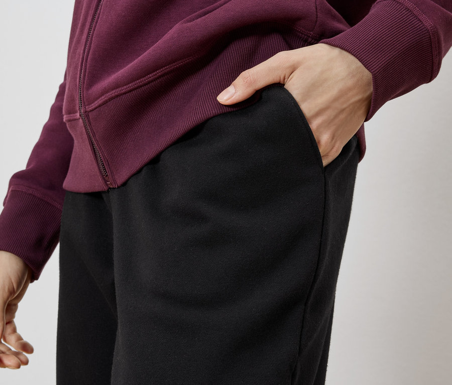 Person mit Hand in der Tasche einer schwarzen Hose, trägt eine bordeauxrote Jacke.