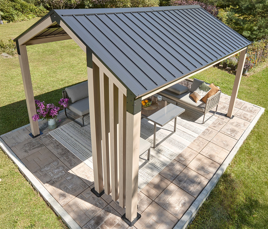 Draufsicht auf einen Pavillon mit graubraunem Dach, hellbraunen Holzpfosten und grauen Terrassenmöbeln auf einer Terrasse.