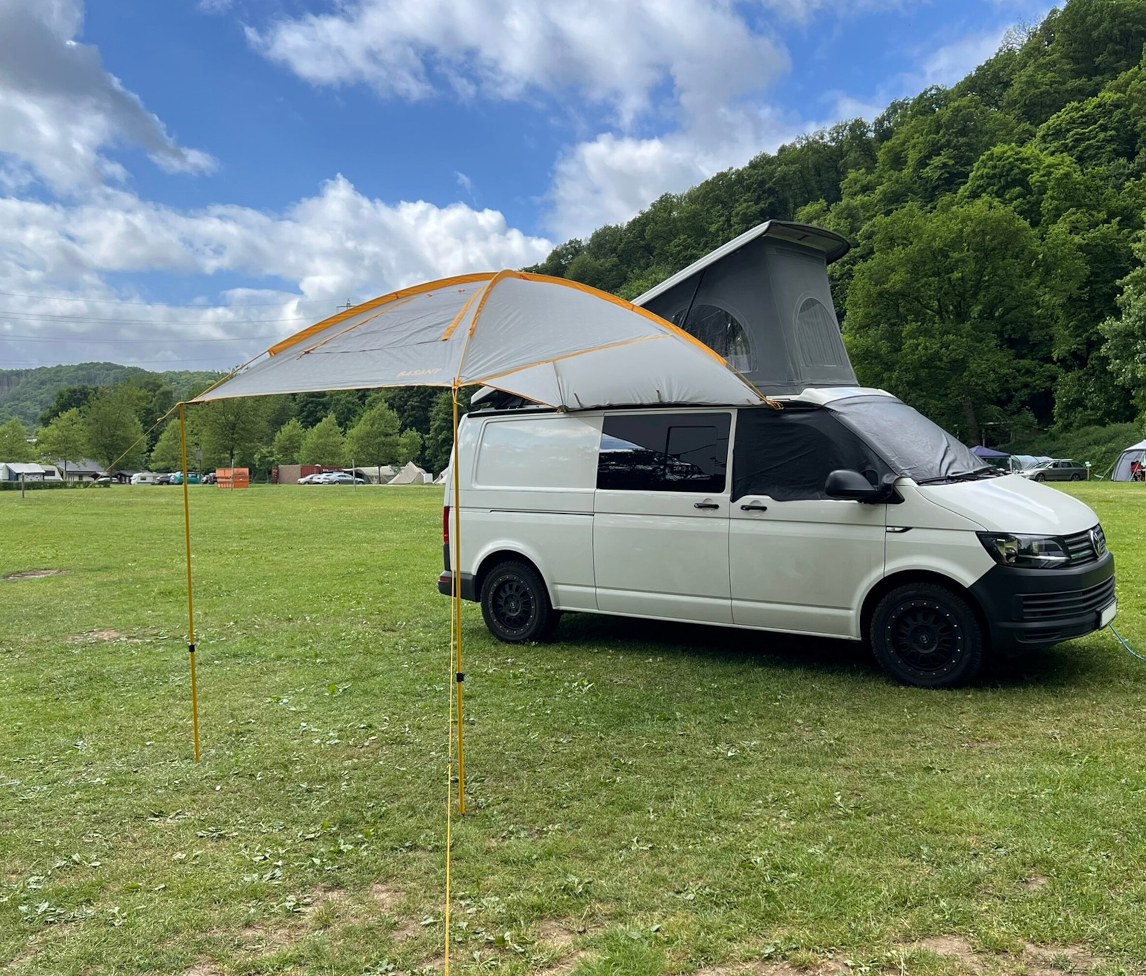 Weißer Van mit aufgeklapptem Dach und Tambu Sonnensegel »BASANT« auf einer Wiese.