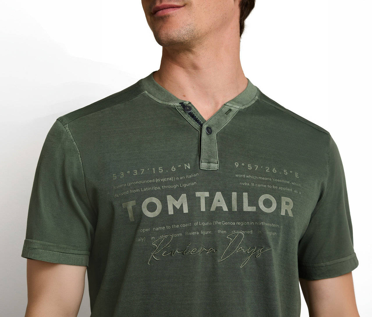 Mann trägt ein grünes Kurzarm-T-Shirt mit Henley-Ausschnitt. Auf dem Shirt sind die Schriftzüge „TOM TAILOR“ und „Riviera Days“ sowie weitere beschreibende Texte zu sehen.