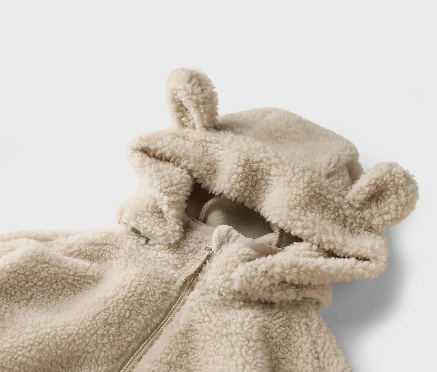 Nahaufnahme einer hellbraunen, flauschigen Jacke mit Kapuze und Ohren auf einem weißen Hintergrund.