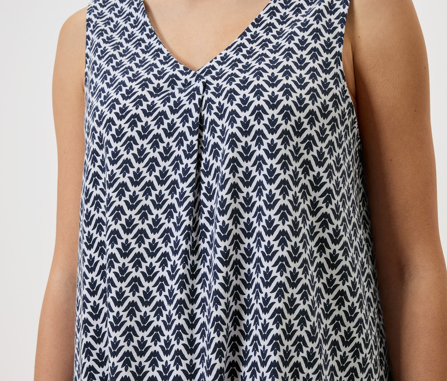 Nahaufnahme einer Frau, die ein ärmelloses Kleid mit blau-weissem Muster trägt.