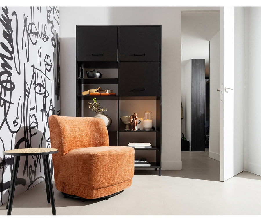 Ein orangefarbener Sessel steht vor einem schwarzen Regal, daneben ein kleiner runder Beistelltisch. Die Wand hinter dem Sessel ist mit schwarz-weißer abstrakter Kunst verziert. Eine offene Tür führt rechts in einen anderen Raum.