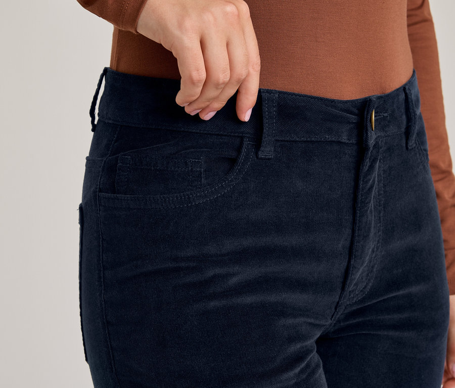 Hand, die den Bund einer dunkelblauen Cordhose anpasst, getragen mit einem braunen Langarmshirt.