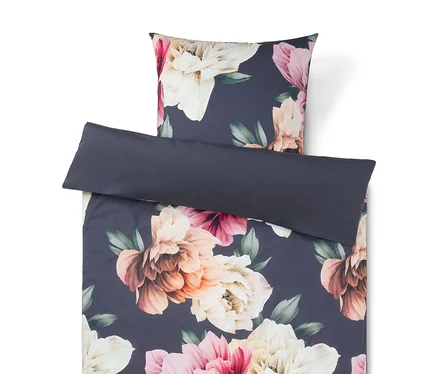 Bettwäsche-Set mit floralem Muster auf dunkelblauem Hintergrund mit großen rosa, cremefarbenen und pfirsichfarbenen Blüten. Ein schlichtes dunkelblaues Kissen liegt obenauf.