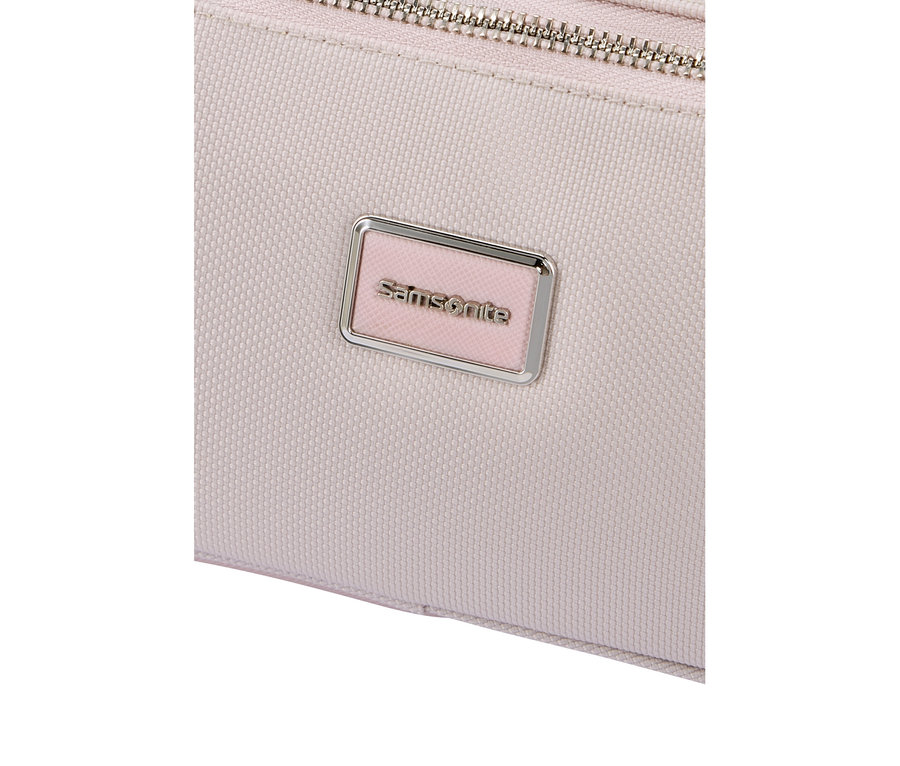 Nahaufnahme eines hellrosa strukturierten Stoffartikels mit einem silbernen Reißverschluss oben und einem rechteckigen, silbergerahmten Samsonite-Logo-Schild mit hellrosa Hintergrund.
