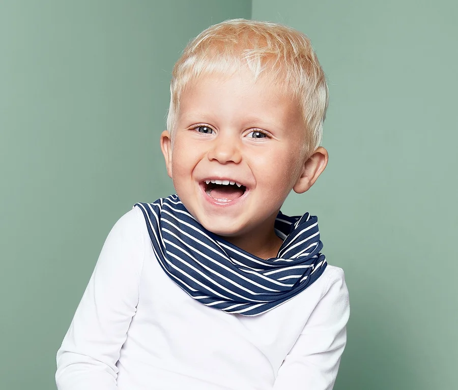 Lächelnder kleiner Junge sitzt und trägt ein Multifunktionstuch mit blauen Streifen.