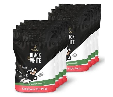 Acht schwarz-weiße Tchibo Black & White Pads Maxipacks, 8 x 100 Pads, sind in zwei Reihen gestapelt. Die Packungen haben einen schwarzen oberen Teil, einen weißen unteren Teil, einen grünen Streifen und eine rote Basis.