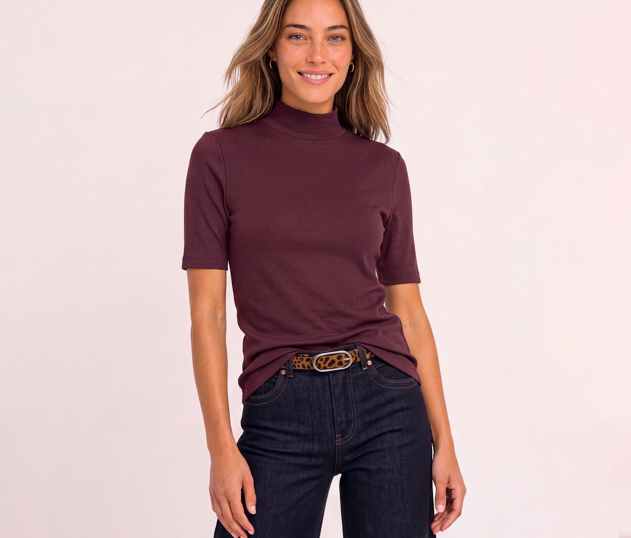 Lächelnde Frau trägt ein rotes, geripptes Street One Shirt mit Stehkragen und kurzen Ärmeln, dunkle Jeans und einen Gürtel mit Leopardenmuster.