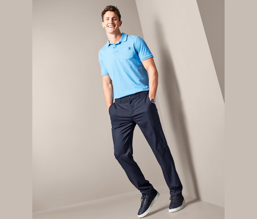 Mann posiert in blauem Poloshirt und dunkelblauen Chino.