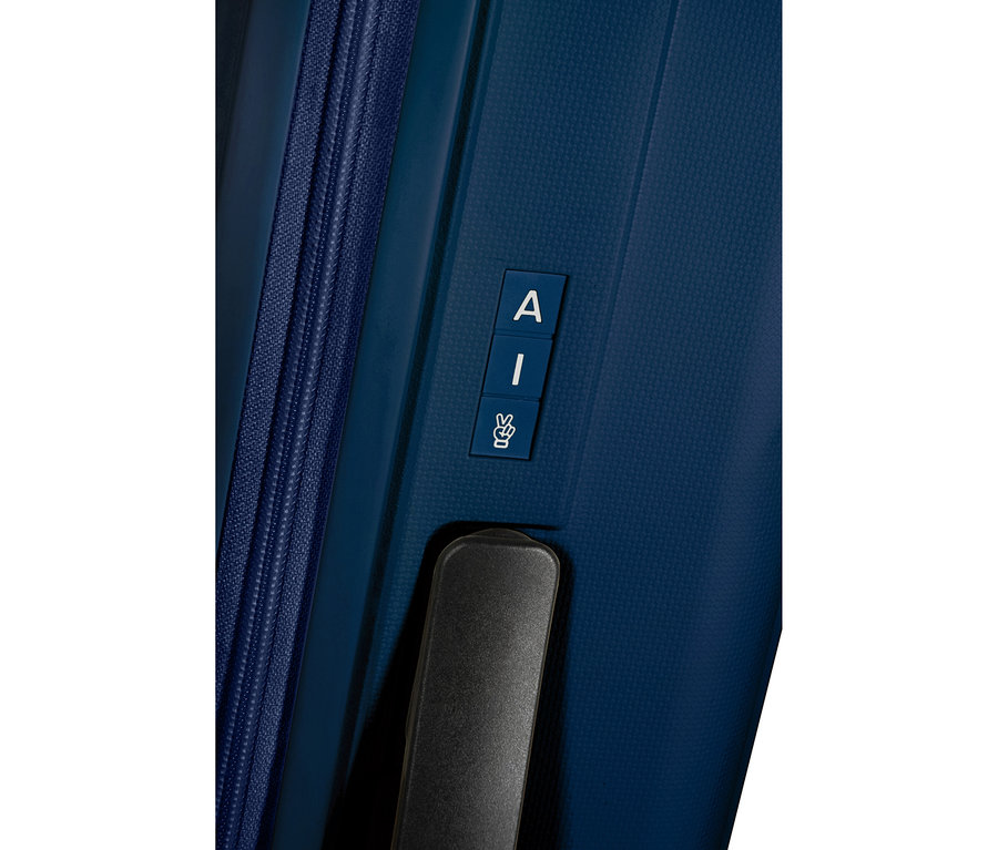 Nahaufnahme eines navyblauen American Tourister »Rejoy Spinner« Koffers mit Reißverschluss, schwarzem Griff und drei blauen Etiketten mit den weißen Buchstaben „A“, „I“ und einem Peace-Zeichen.