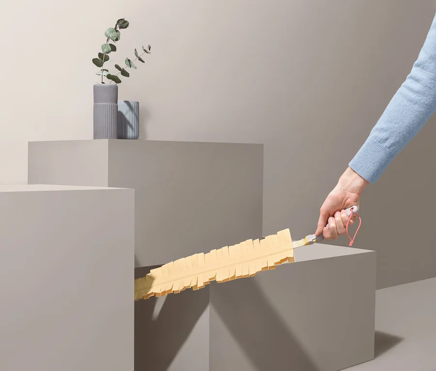 Eine Hand hält ein Staubschwert und -wedel zwischen zwei grauen Würfeln.