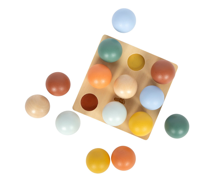 Hellbraunes Holzbrett mit neun runden Vertiefungen, zwei davon mit dunkelbraunen und gelben Kugeln gefüllt. Bunte Holzkugeln in Hellblau, Türkis, Orange, Hellbraun, Hellbeige, Gelb und Dunkelbraun liegen auf und um das Brett herum. Das 'small foot'-Logo ist auf dem Brett sichtbar.