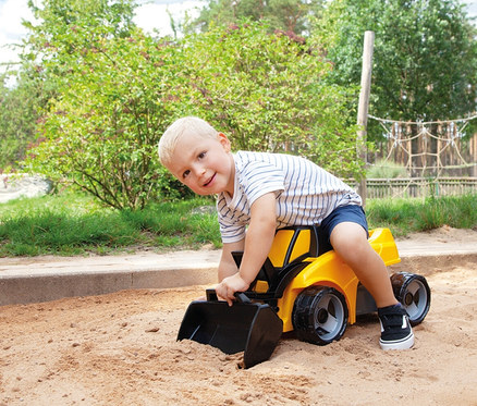 Kleiner Junge sitzt lächelnd auf einem gelben GIGA TRUCKS Aufsitz-Schaufellader "Pro X" und spielt im Sandkasten.
