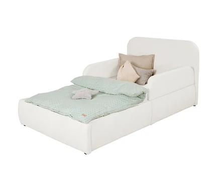Weißes gepolstertes Kinderbett mit Kopf- und Seitenteilen. Eine hellgrüne Steppdecke mit Punktmuster bedeckt die Matratze. Ein graues Sternkissen liegt auf der Decke, drei Zierkissen (beige, hellrosa, grau) lehnen am Kopfteil.