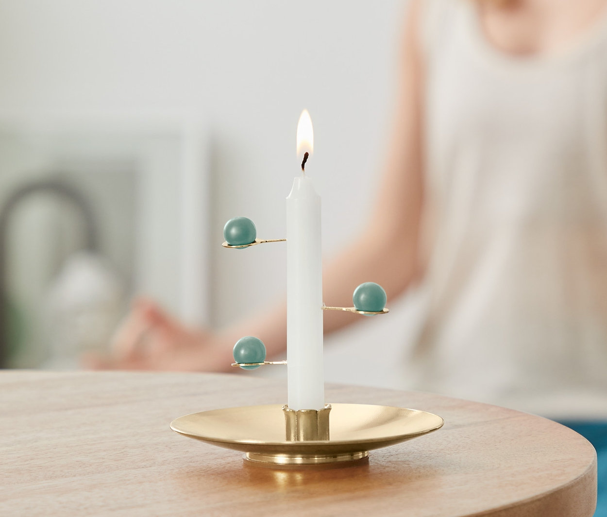 Eine brennende Meditationskerze steht auf einem Tisch, im Hintergrund eine Frau in Meditationshaltung.