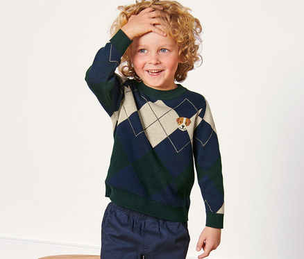 Ein Junge richtet seine Haare und trägt einen Kleinkinder-Strickpullover.